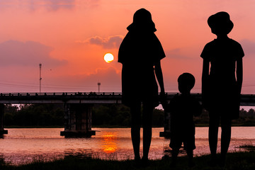 Fototapeta na wymiar silhouette of Three brothers child standing at river and the bridge sunset background and looking forward