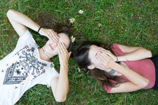 Relaxed young persons (teenage girls) lying in grass and flowers with stretched hand - closed eyes