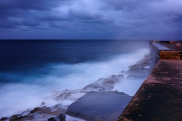 Evening by the walls of the Malecón esplanade in Havana, Cuba and dramatic sea bounding water on the rocks.