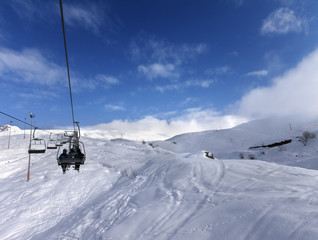 Fototapeta na wymiar Chair-lift and off-piste slope in wind day
