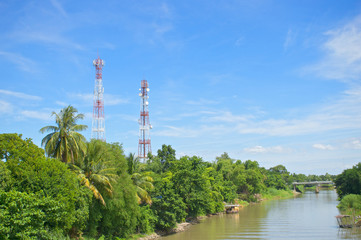 Obraz premium Antenna cellular tower in forest beside river and blue sky