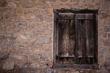 Fototapeta na wymiar Boarded up wooden window shutter and weathered wall of derelict house.