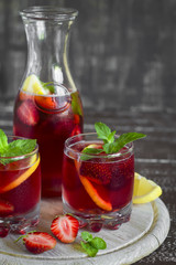 strawberry lemonade with fresh mint and lemon in glass beakers on a dark wooden background