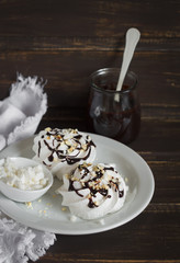 meringue with chocolate sauce and nuts on a white plate on a dark wooden background