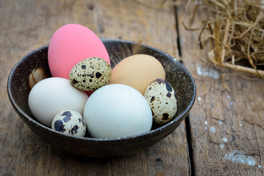 Different types of eggs in bowl on wood background