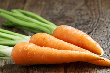 Fresh carrots with tops on old wooden table, selective focus