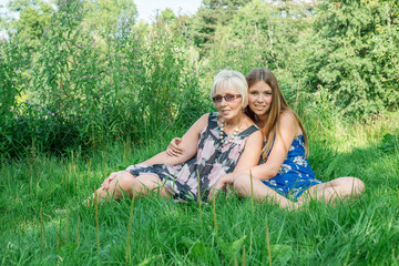 Two women of different generations sitting on the grass in the summer. Mother and daughter hugging. Grandmother and granddaughter.