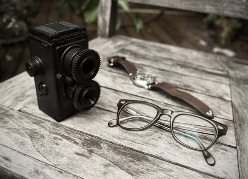 Vintage retro camera, eyeglasses and watch on wooden background