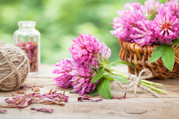 Bunch of clover and basket with flowers on wooden table.