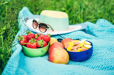 Picnic sheet with fruits on the grass, hat with sunglasses on ba