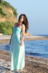 Fototapeta na wymiar Portrait of woman at the beach wearing long coral dress