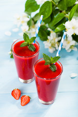 Strawberry smoothie and flower petals on blue background