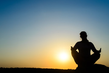 Woman meditating in front of the rising sun