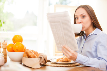 Businesswoman is reading the newspaper while having breakfast