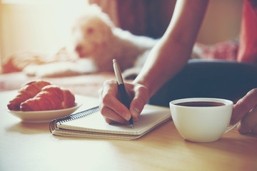 female hands with pen writing on notebook with morning coffee an