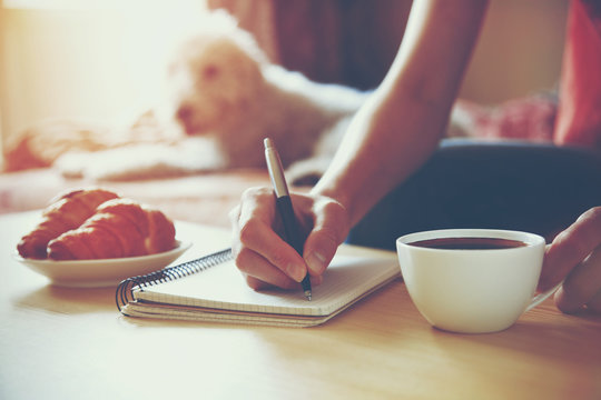 female hands with pen writing on notebook with morning coffee an