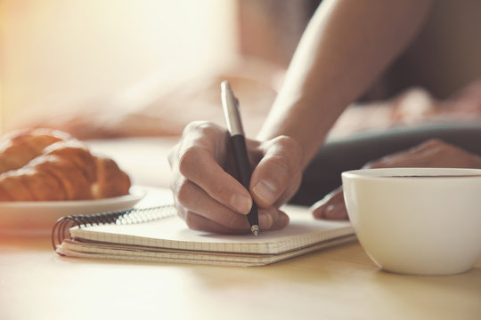 female hands with pen writing on notebook with morning coffee an