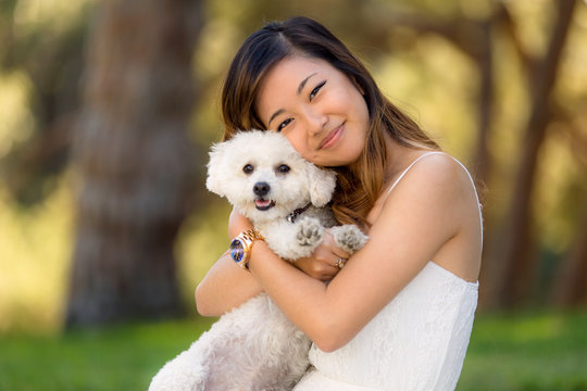 Beautiful woman with white dog smiling and hugging at the park