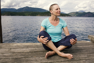 Fototapeta na wymiar Middle aged woman whose hair is growing back after chemotherapy sitting on a dock