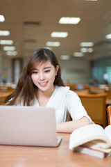 Asian beautiful female student study in library with laptop