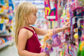 Adorable girl select dolls in toy section of supermarket