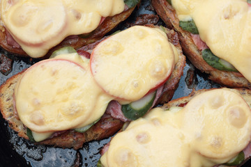 Freshly grilled slice of bread with pickles, tomatoes, ham and melted cheese.