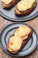 Freshly grilled slice of bread with pickles, tomatoes, ham and melted cheese.