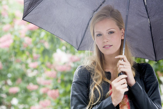 Beautiful, blond girl with umbrella. Trees on background