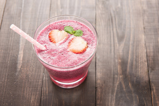 Strawberry fruit smoothies with straw on wooden background.