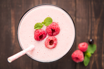 Raspberry fruit smoothie with straw on wooden background.
