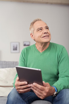 älterer mann sitzt auf dem sofa und hält tablet in der hand