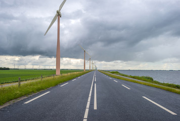 Fototapeta na wymiar Wind farm on a dike along a lake in a cloudy summer