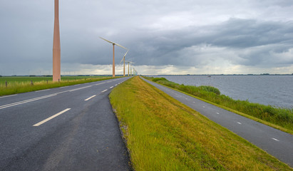 Fototapeta na wymiar Wind farm on a dike along a lake in a cloudy summer