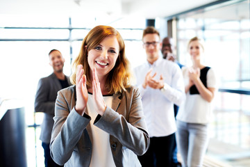 White female executive standing in front of colleagues clapping