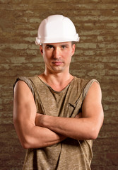 Portrait of a workman in white hardhat against a briсk wall background