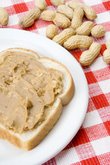 Chunky Peanut Butter on Slice of Bread – A slice of white bread with chunky peanut butter spread. Peanuts in shell in background.