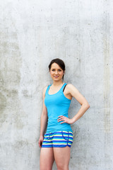 Girl in blue tank top and shorts over the wall smiling.