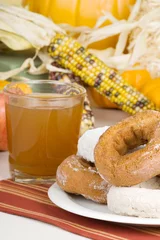 Poster Cider and Doughnuts – A stack of donuts with a glass of apple cider. Autumn decorations in background. © Cathleen