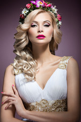 Beautiful blond girl in the image of a bride with flowers in her hair. Beauty face. Wedding image. Picture taken in the studio on a purple background.