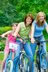 Family Biking Fun – A Mother and Two Daughters ride their bikes on a summer day.