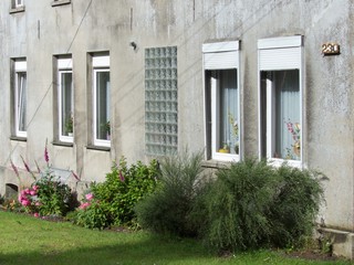 Verwitterte graue Fassade eines Wohnhaus mit vielen Fenstern im Sommer bei Sonnenschein in...