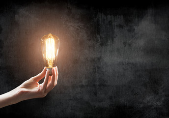 hand holding Light bulb on blackboard background