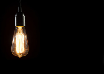 A classic Edison light bulb on black background with space for text - obrazy, fototapety, plakaty