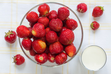 Ripe strawberries in the glass bowl with glass of milk