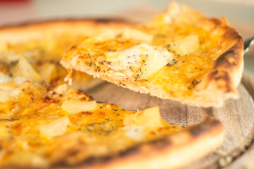 Baked cut pizza with pineapple and meat on wooden board