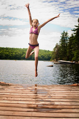 Fototapeta na wymiar young teenage girl jumping off a dock at a lake in Ontario's cottage country