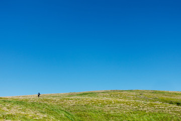 Fototapeta premium Hiker on the green plain under blue skies