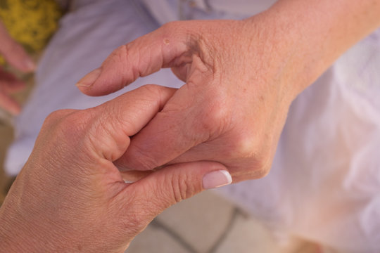 Hands of an elderly woman holding the hand of a younger woman.