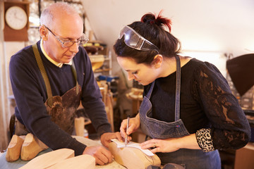 Senior shoemaker training apprentice to make shoe lasts - obrazy, fototapety, plakaty