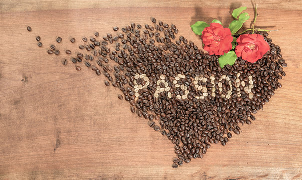 Chicchi di caffè con rose rosse, disposti in forma di cuore su un piano di legno grezzo.Scritta con chicchi di caffè crudo.